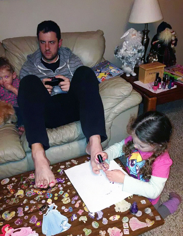 Татко позволява на дъщеря си да му лакира ноктите на краката, докато той си играе на видео игри